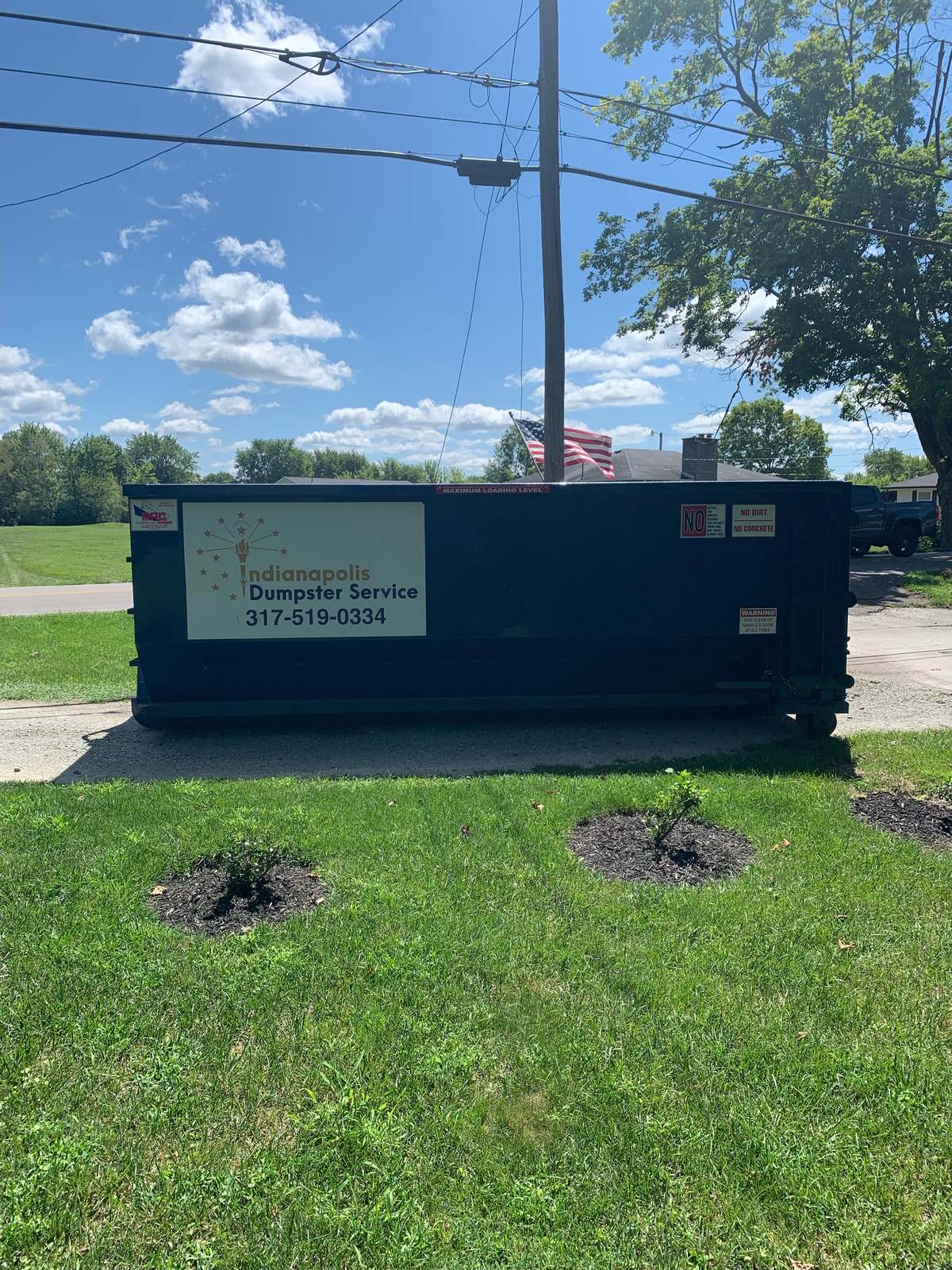 A navy Indianapolis Dumpster Service roll-off dumpster beside a lawn