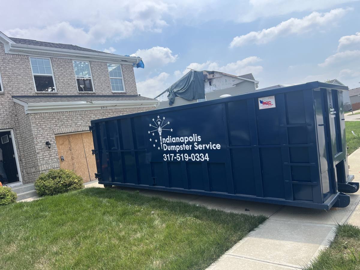 A navy Indianapolis Dumpster Service roll off container. On the driveway of a brick two-story home.