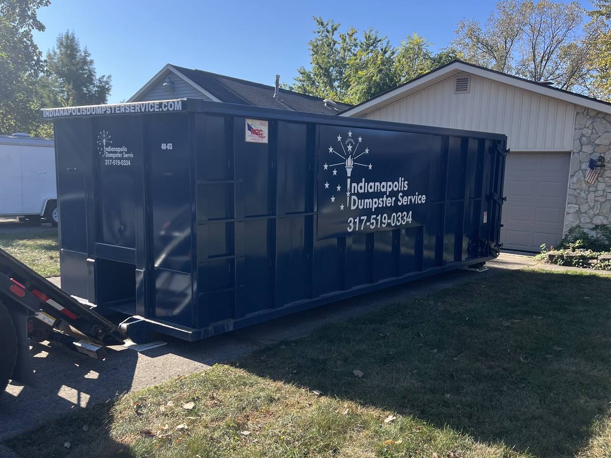 A navy Indianapolis Dumpster Service roll off container. On the driveway of a ranch home.