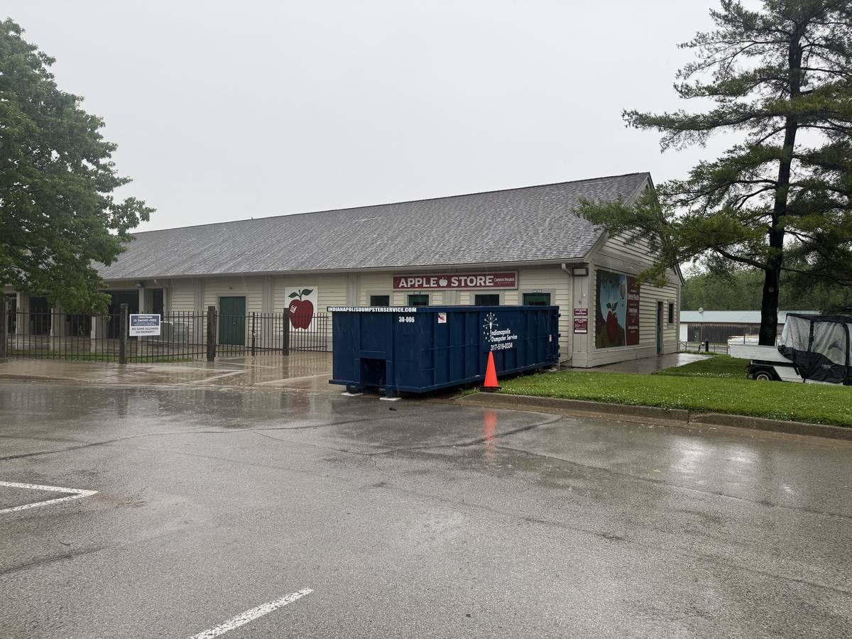 A navy Indianapolis Dumpster Service roll off container. In front of a store on a rainy day.