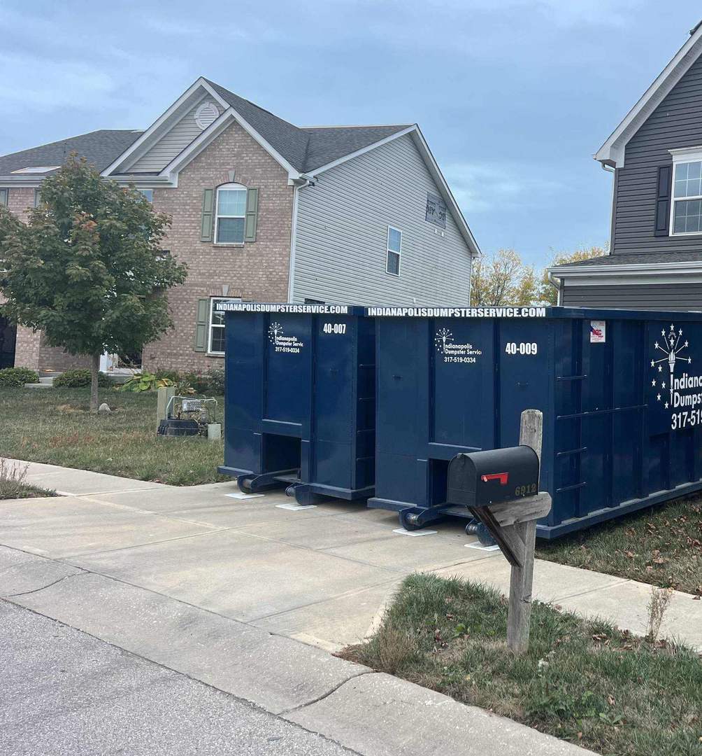 A navy Indianapolis Dumpster Service roll off container. Two dumpsters on one driveway, set on pads.