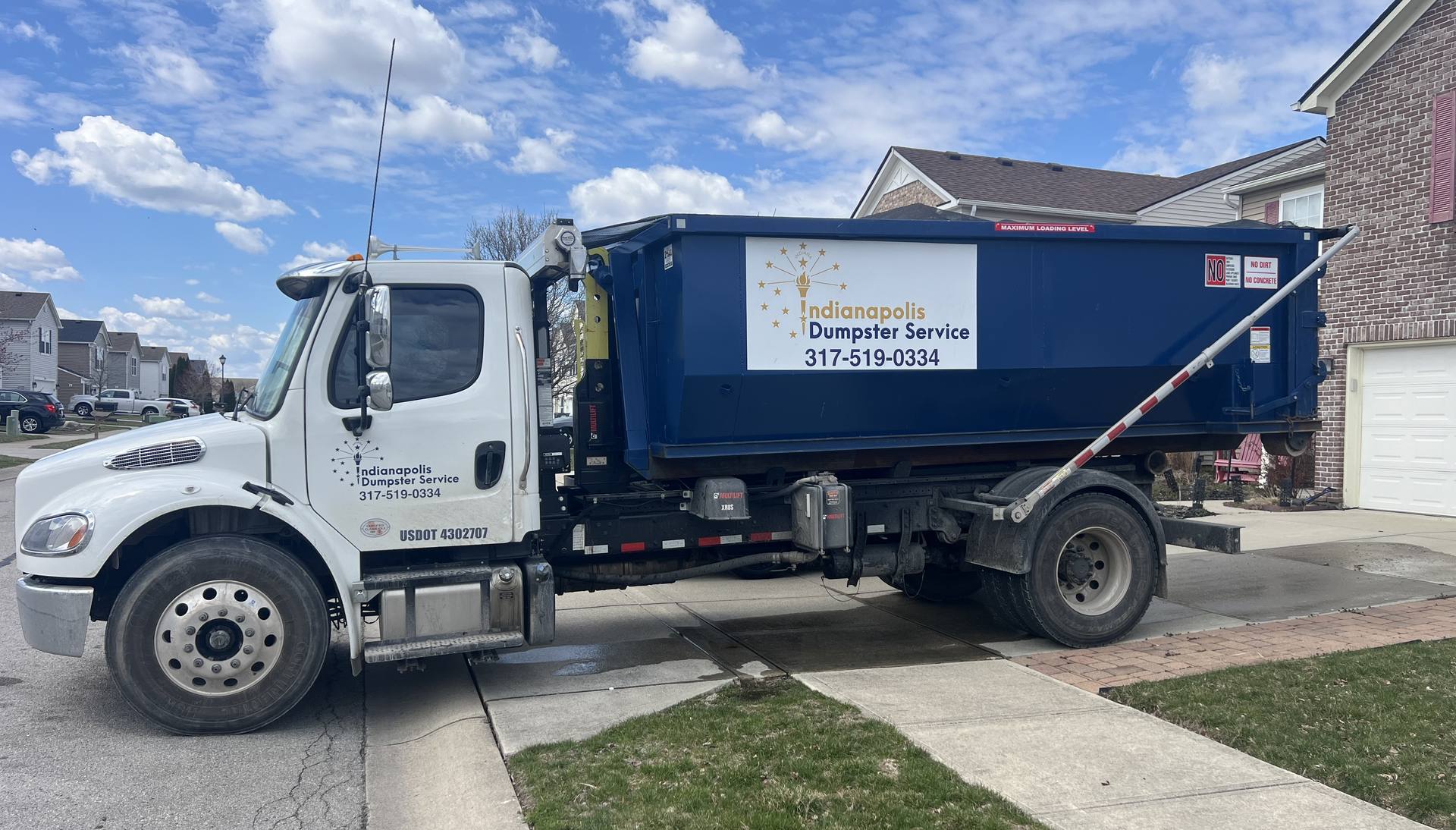 A navy Indianapolis Dumpster Service roll off container. Our truck setting a dumpster on a home driveway.