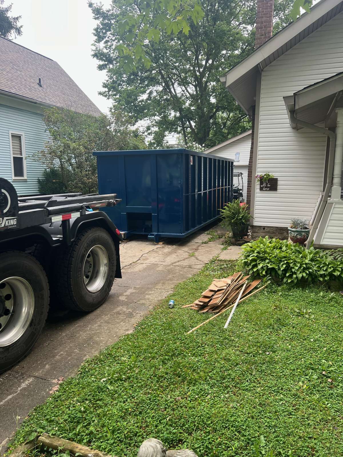 A navy Indianapolis Dumpster Service roll off container in Arcadia. Set beside a home's side drive, with our truck still in the driveway.