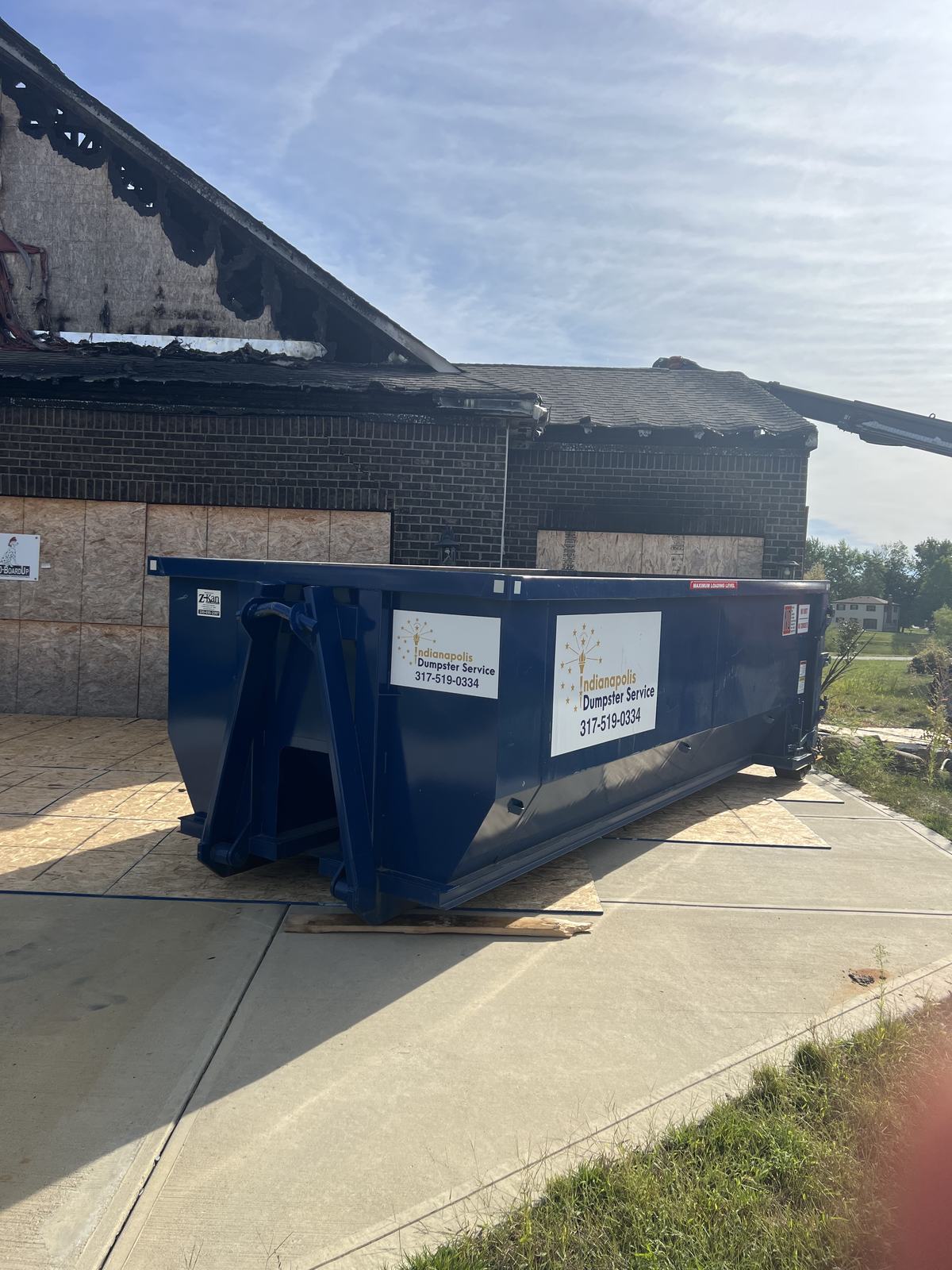 A navy Indianapolis Dumpster Service roll off container. In front of an open garage on a brick home.