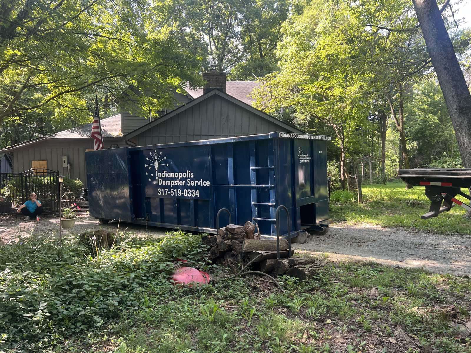A navy Indianapolis Dumpster Service roll off container in Carmel. A large dumpster along the side of the driveway, garage still open.