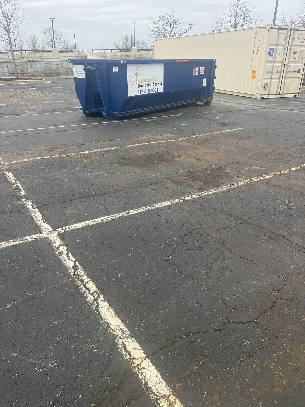 A navy Indianapolis Dumpster Service roll off container in Carmel. In a commercial parking lot.