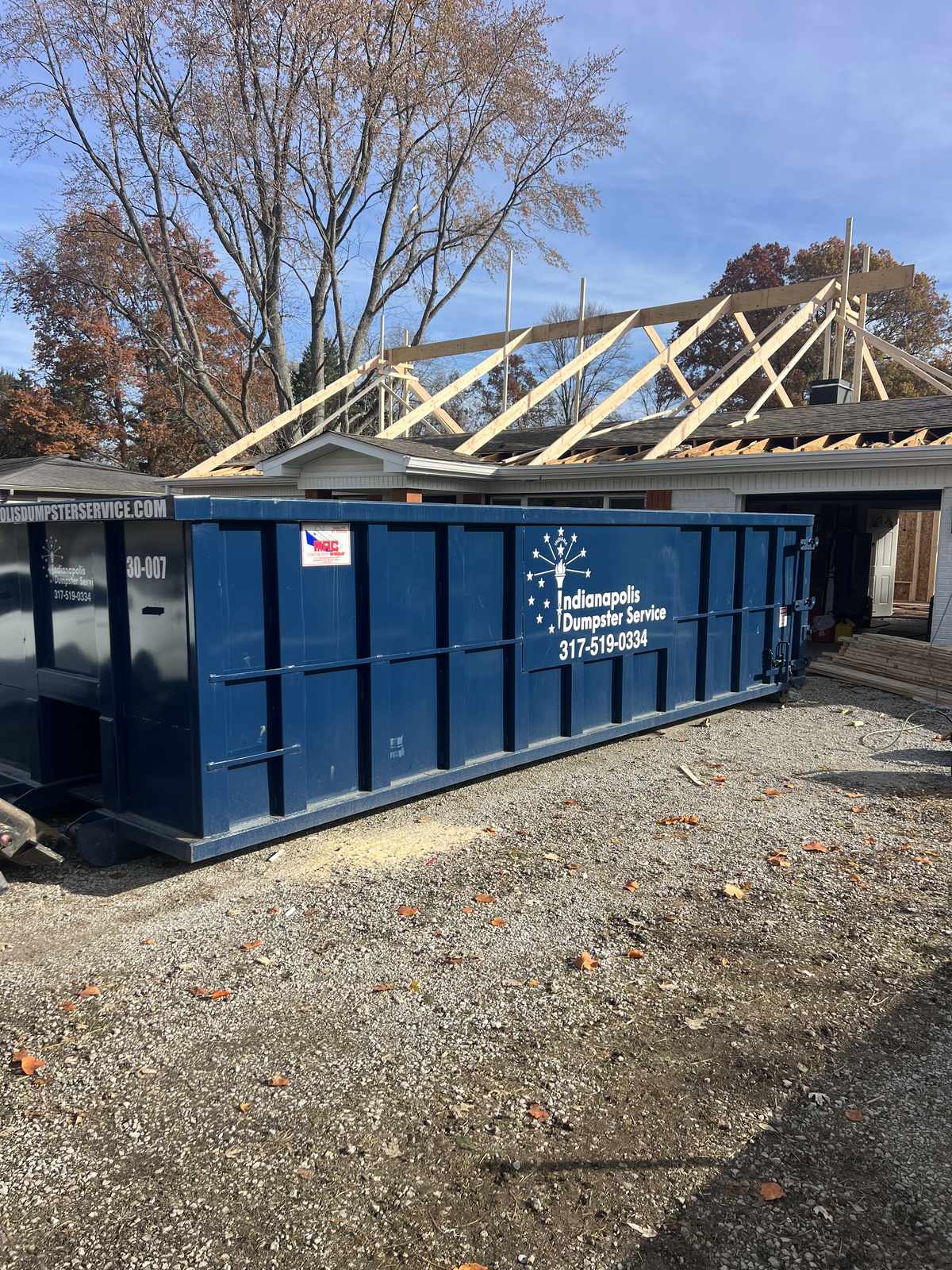 A navy Indianapolis Dumpster Service roll off container in Carmel. A roof tear-off with the dumpster close to the house.