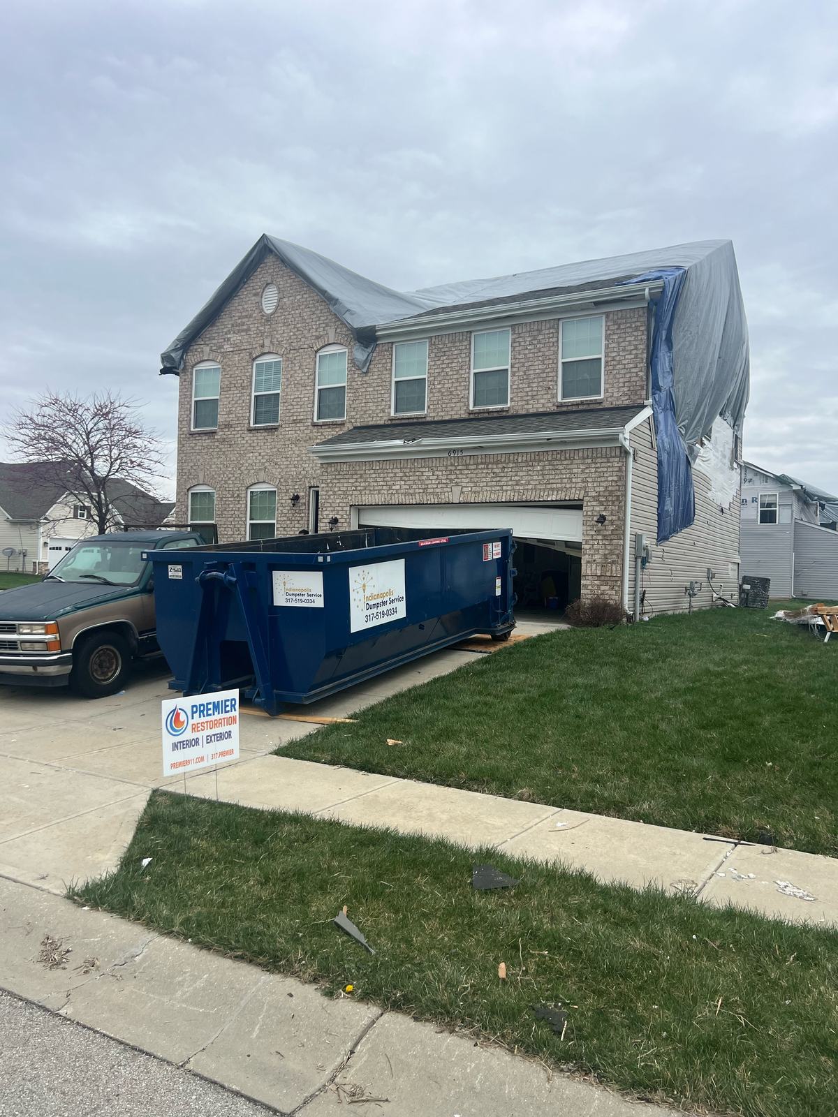 A navy Indianapolis Dumpster Service roll off container in Carmel. Along the side of the house.