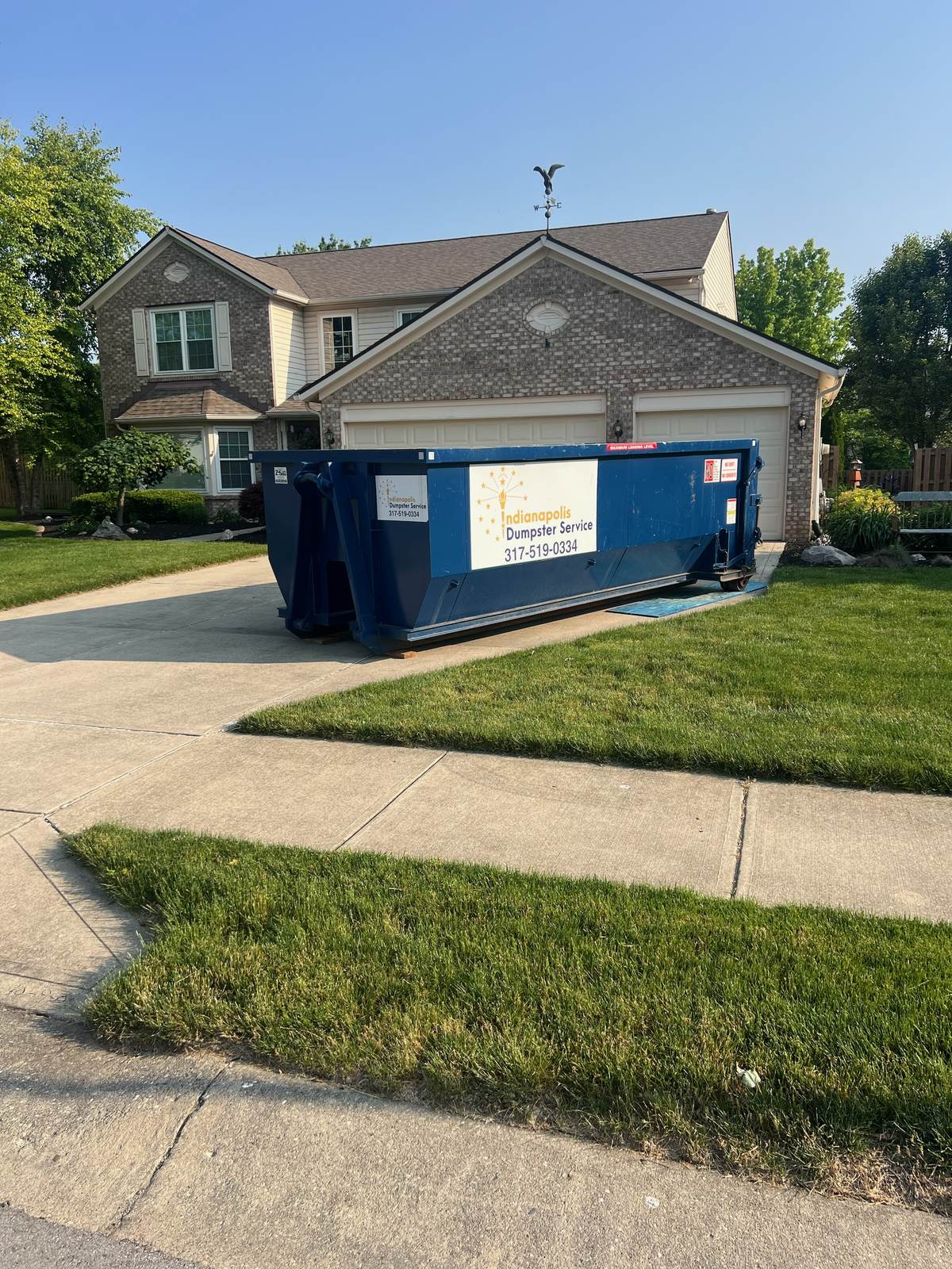 A navy Indianapolis Dumpster Service roll off container in Carmel. Beside a two-story home.