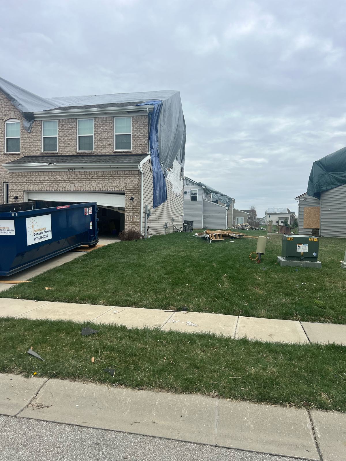 A navy Indianapolis Dumpster Service roll off container in Carmel. In front of a white house.