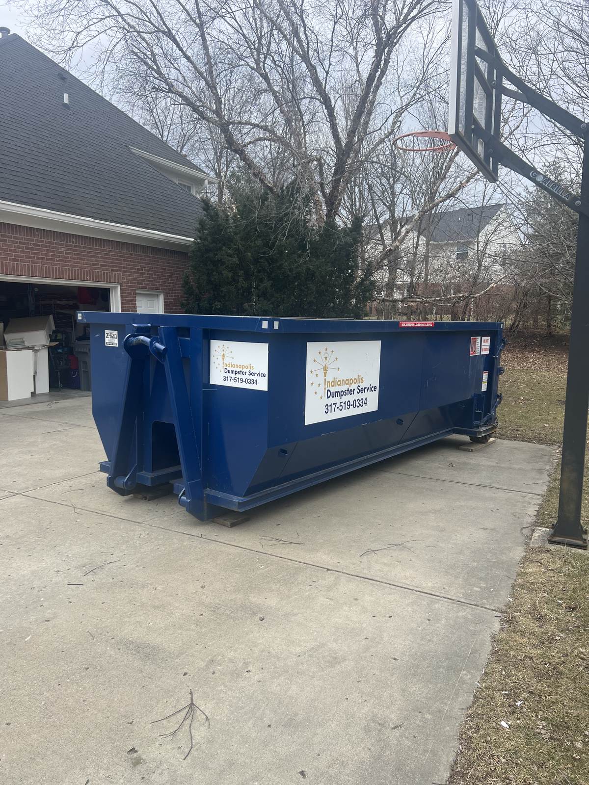 A navy Indianapolis Dumpster Service roll off container in Carmel. A cleanout on a wooded lot.