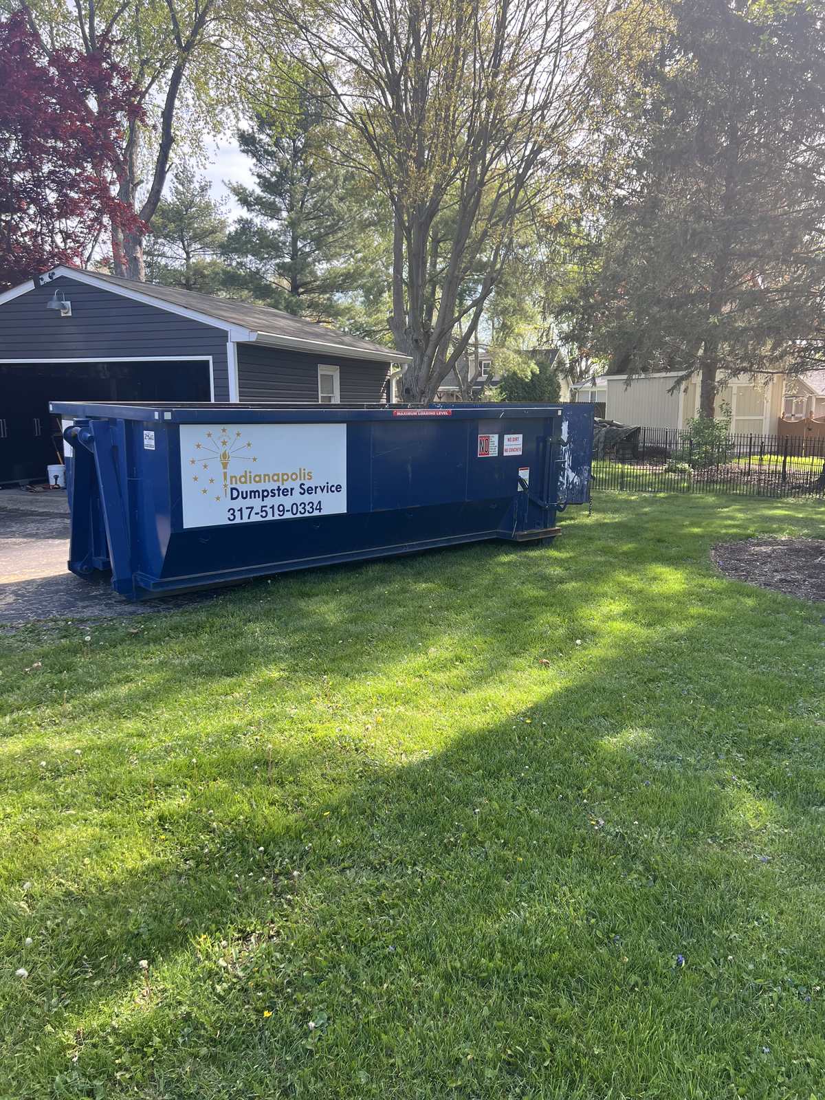 A navy Indianapolis Dumpster Service roll off container in Cicero. On the lawn in front of a detached garage.