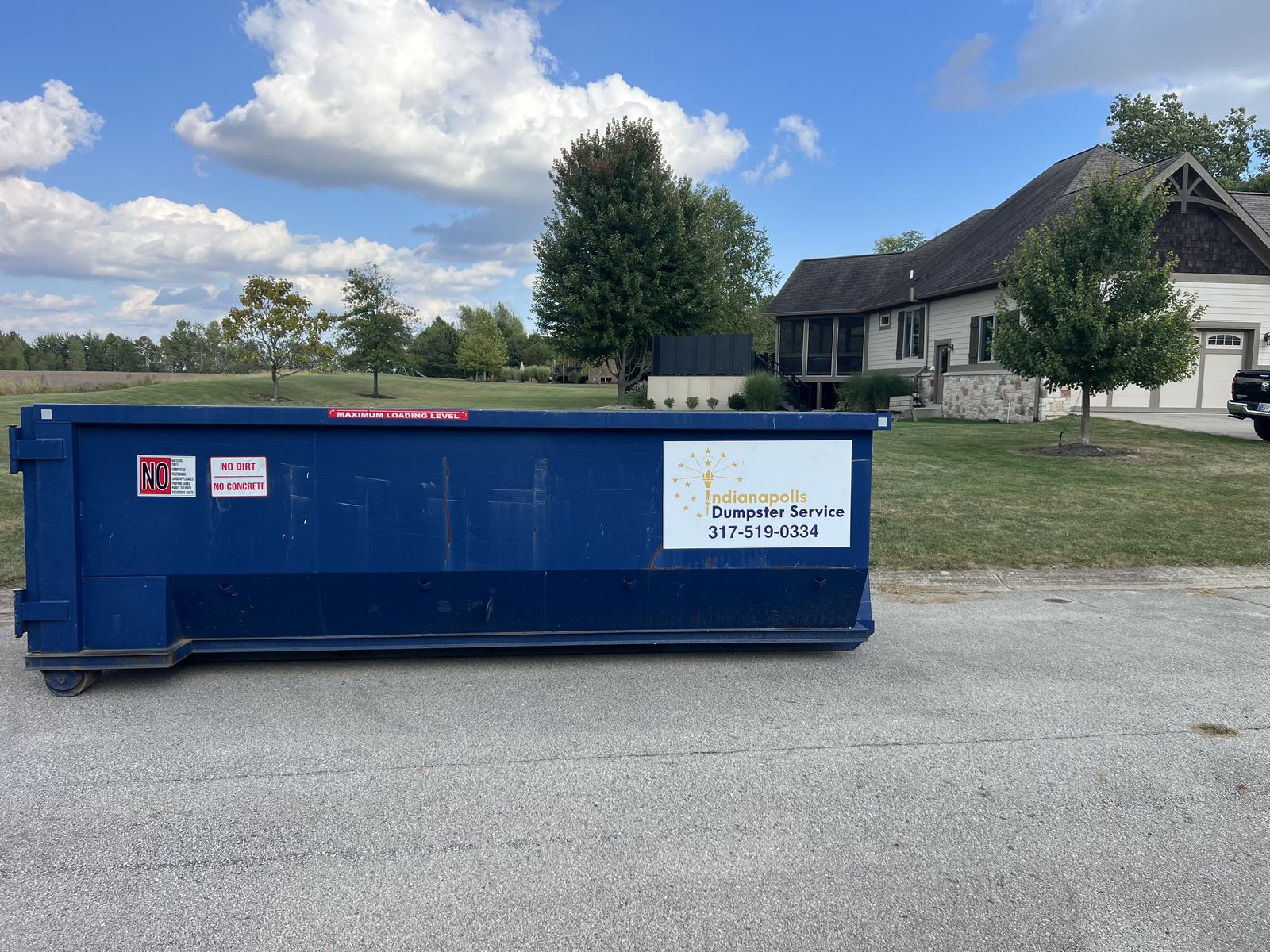A navy Indianapolis Dumpster Service roll off container in Cicero. On open ground next to a new home.