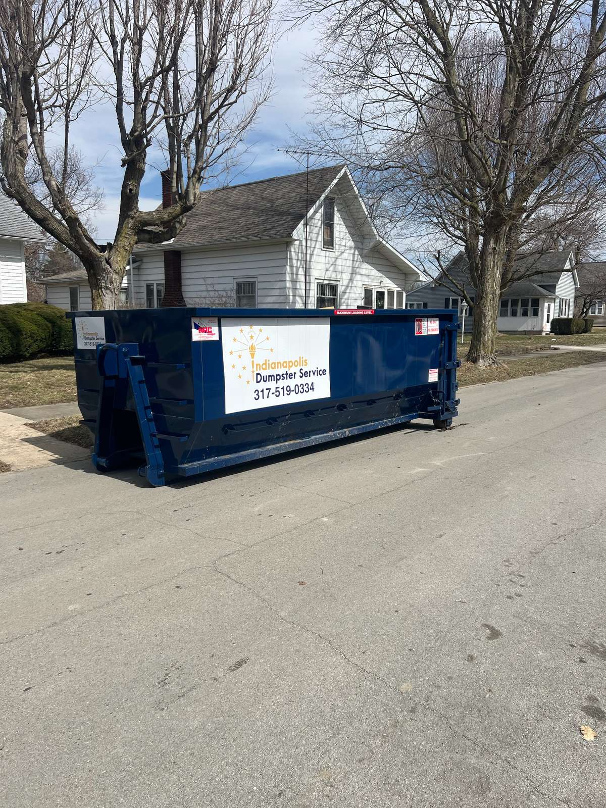 A navy Indianapolis Dumpster Service roll off container in Elwood. Set at the curb on a residential street.