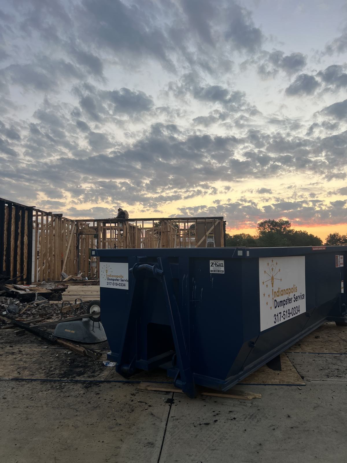 A navy Indianapolis Dumpster Service roll off container. Fence and deck boards being torn out.