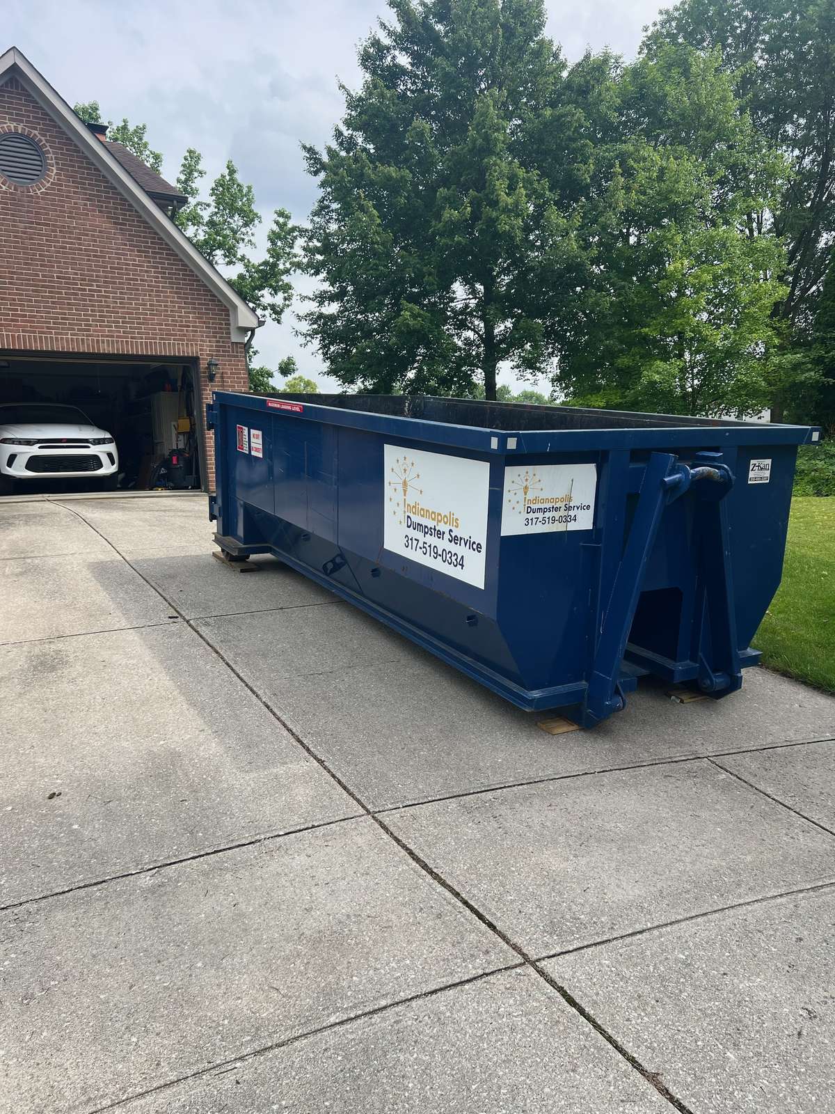 A navy Indianapolis Dumpster Service roll off container in Indianapolis. Beside a carport.