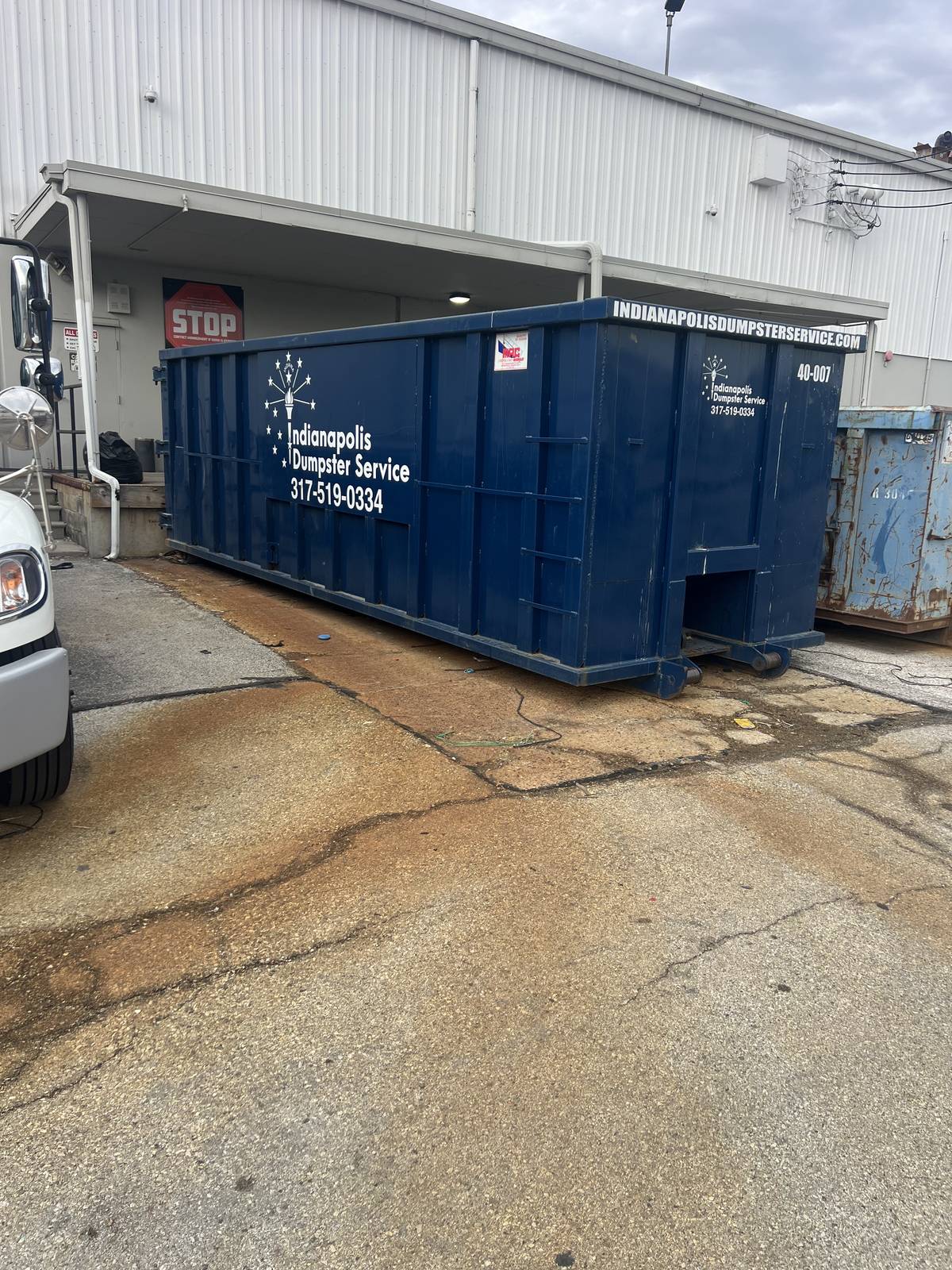 A navy Indianapolis Dumpster Service roll off container in Indianapolis. Beside the loading dock at a commercial building.