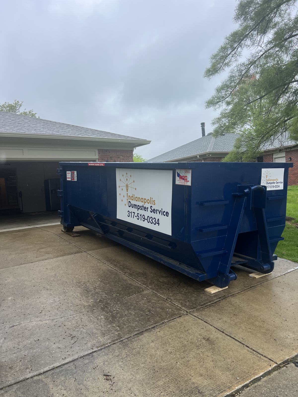 A navy Indianapolis Dumpster Service roll off container in Indianapolis. On an older concrete driveway.