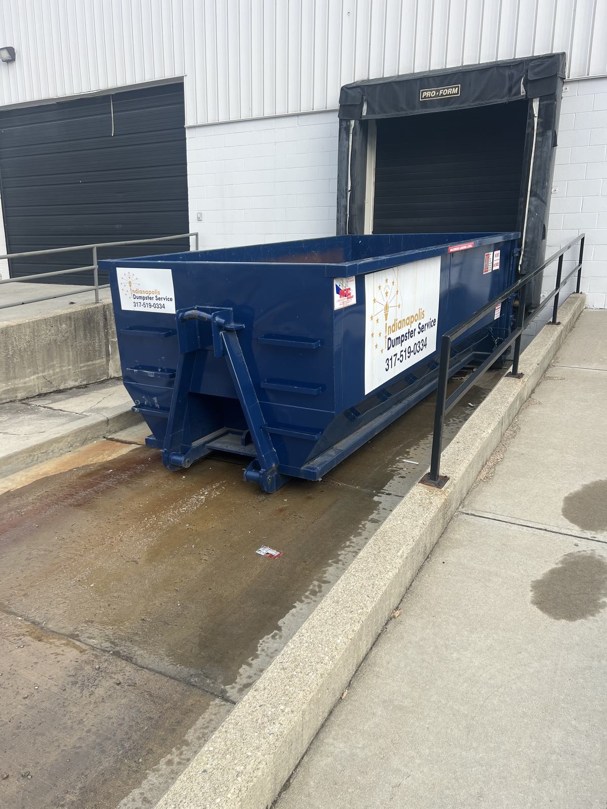 A navy Indianapolis Dumpster Service roll off container in Indianapolis. Backed up to a loading dock.