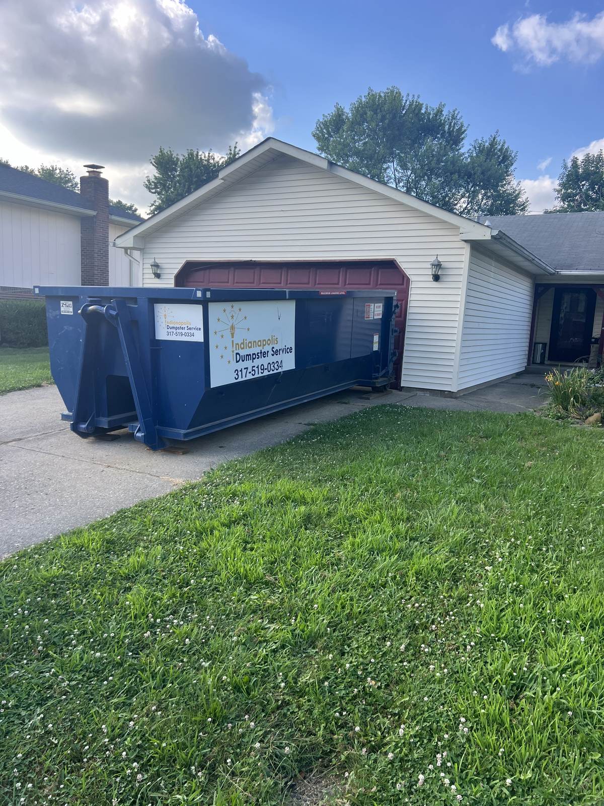 A navy Indianapolis Dumpster Service roll off container in Indianapolis. In front of a two-car garage.