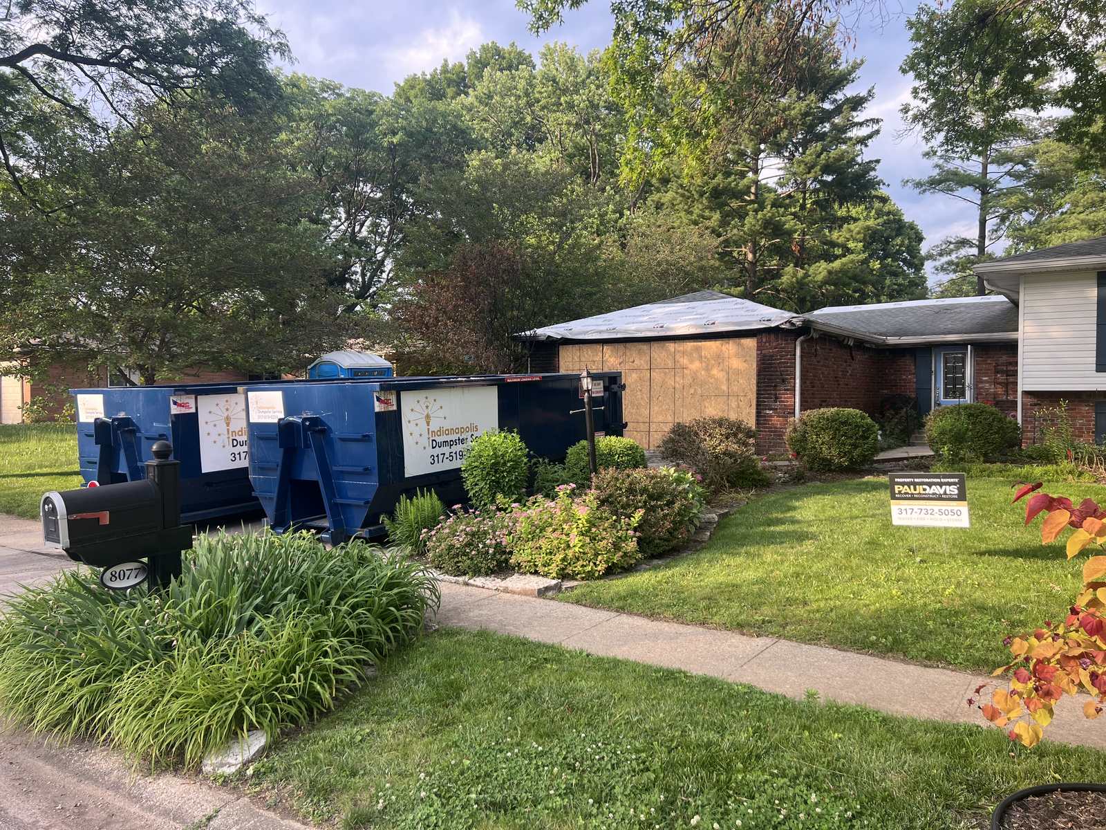 A navy Indianapolis Dumpster Service roll off container in Indianapolis. Two dumpsters at the curb in front of a bungalow.