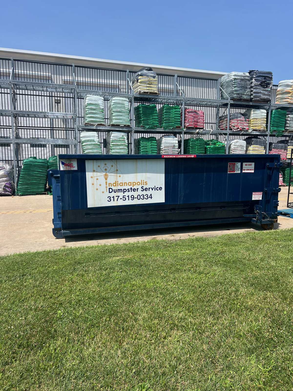 A navy Indianapolis Dumpster Service roll off container in Indianapolis. At a garden center, set against the outdoor racks.
