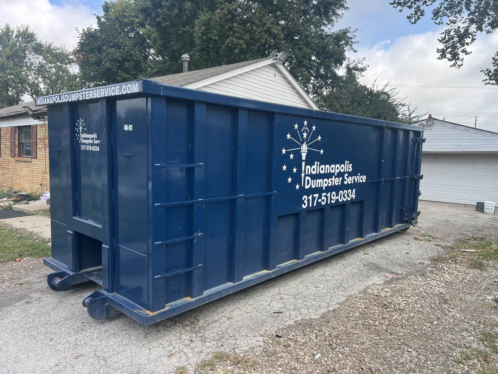 A navy Indianapolis Dumpster Service roll off container in Indianapolis. On gravel beside a house under construction.