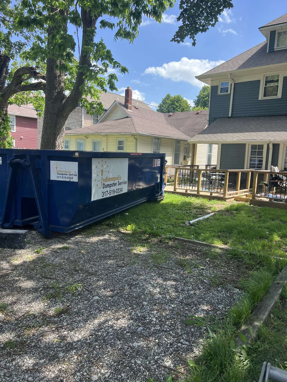 A navy Indianapolis Dumpster Service roll off container in Indianapolis. On the gravel beside the house.