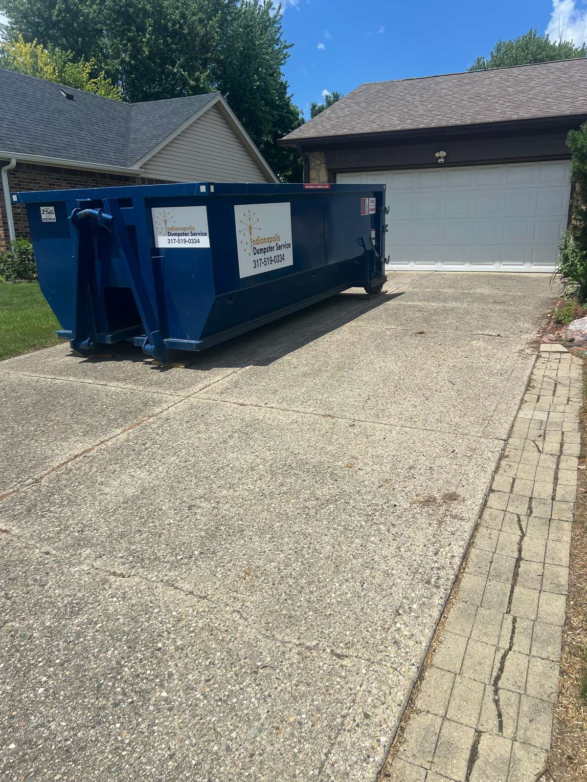 A navy Indianapolis Dumpster Service roll off container in Indianapolis. At the curb in front of a hedge.