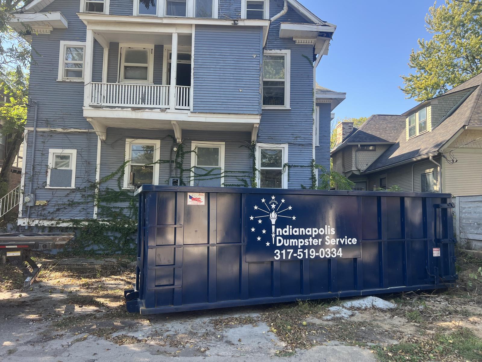A navy Indianapolis Dumpster Service roll off container in Indianapolis. In front of a house flip, ready for the renovation debris.