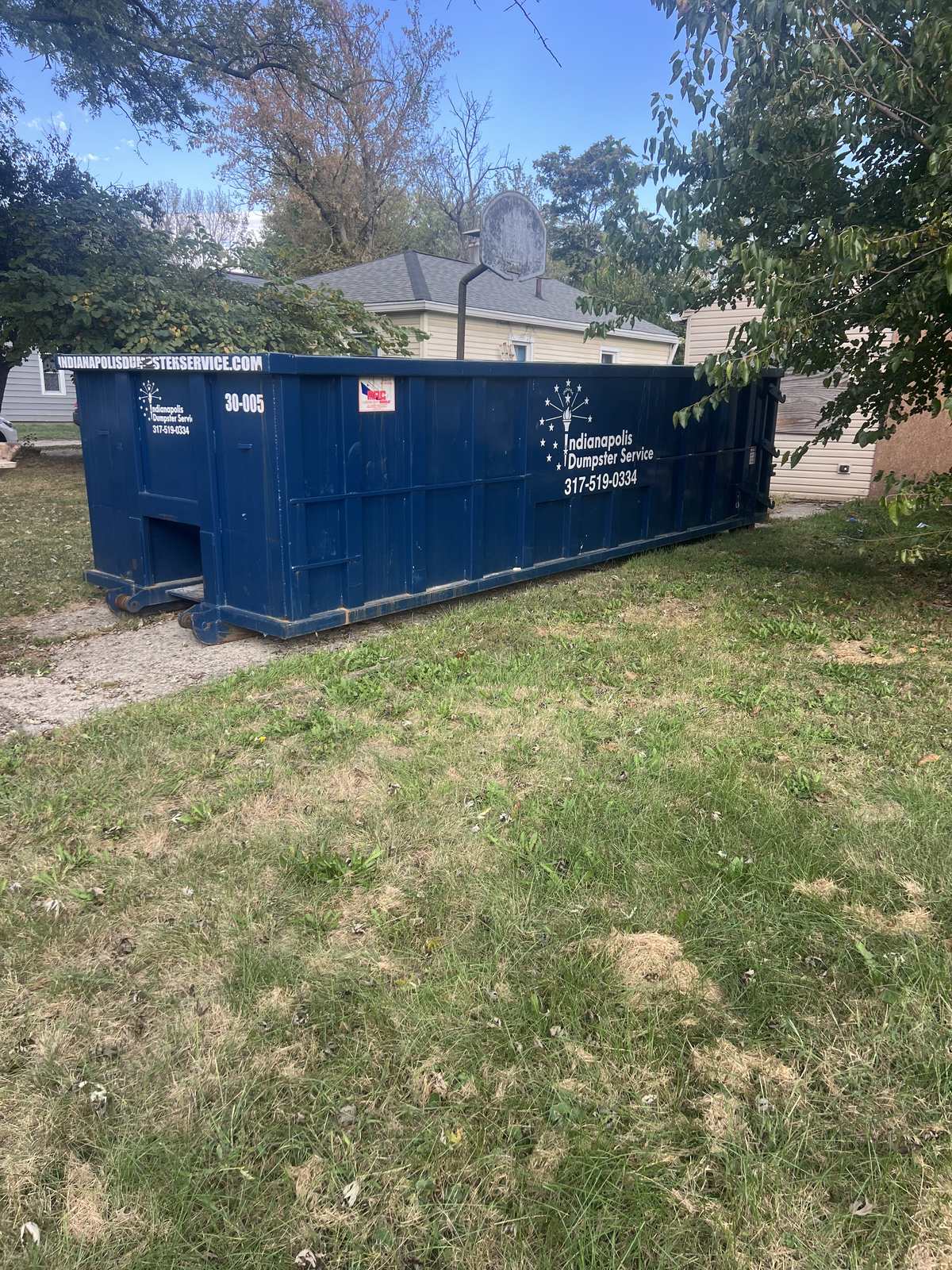 A navy Indianapolis Dumpster Service roll off container in Indianapolis. In the side yard of another house flip.