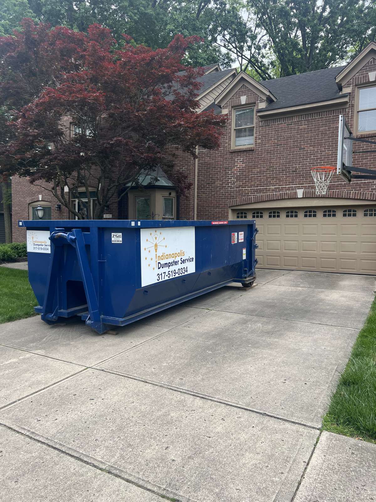 A navy Indianapolis Dumpster Service roll off container in Indianapolis. On a driveway under a red maple.