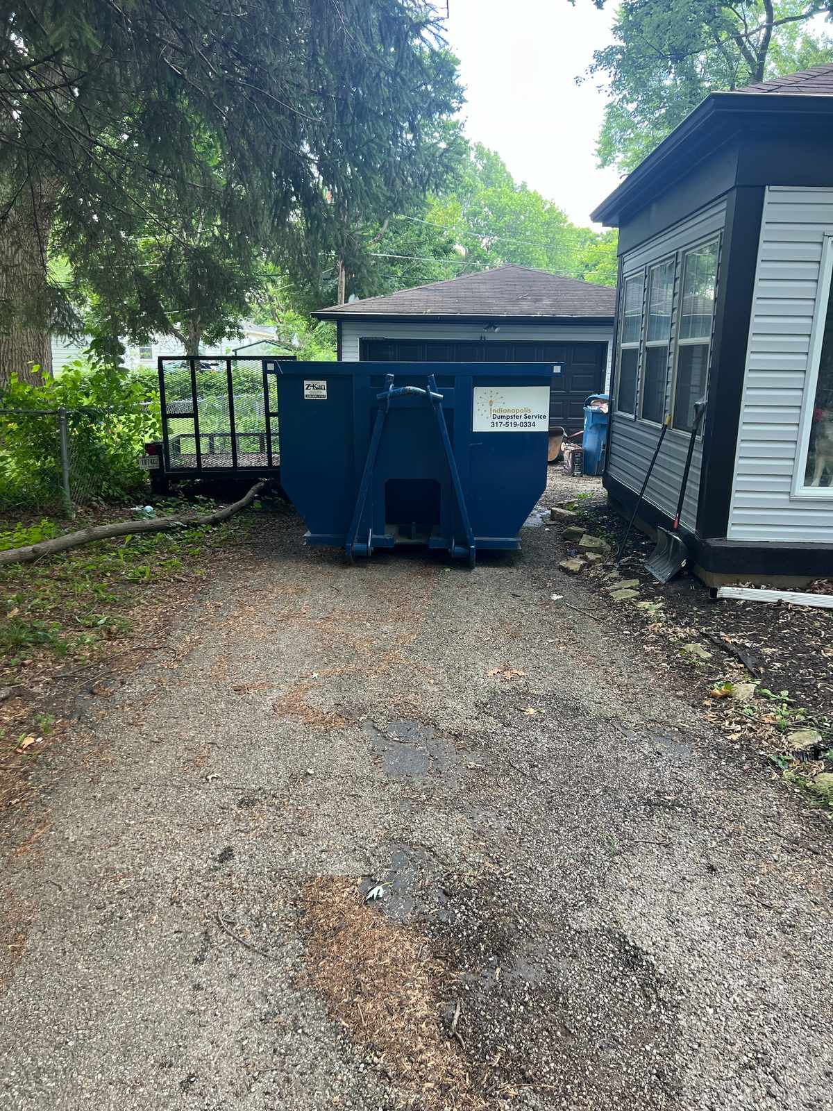 A navy Indianapolis Dumpster Service roll off container in Indianapolis. On a narrow driveway, using the full width.