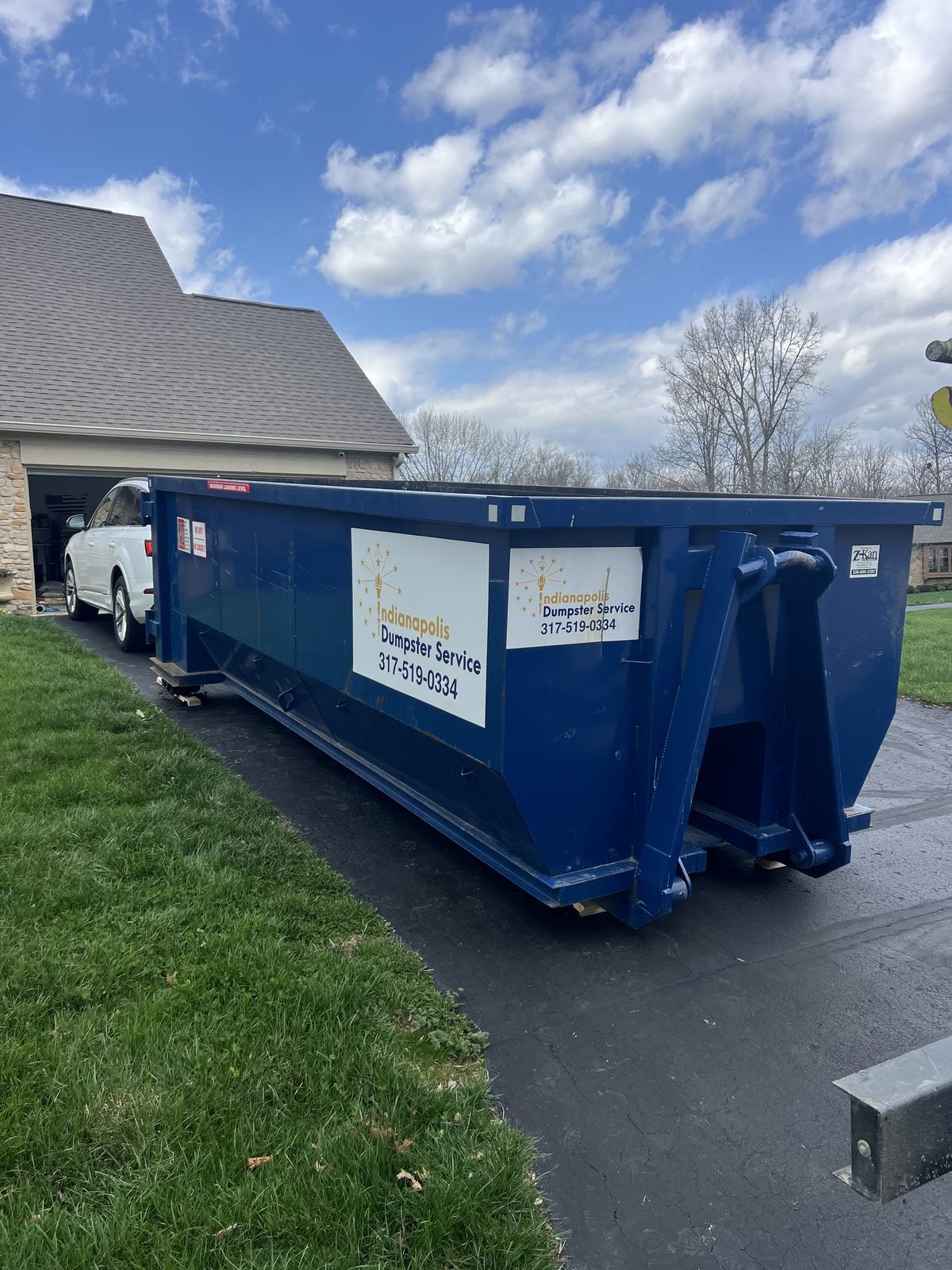 A navy Indianapolis Dumpster Service roll off container in Indianapolis. In front of an open garage during a cleanout.