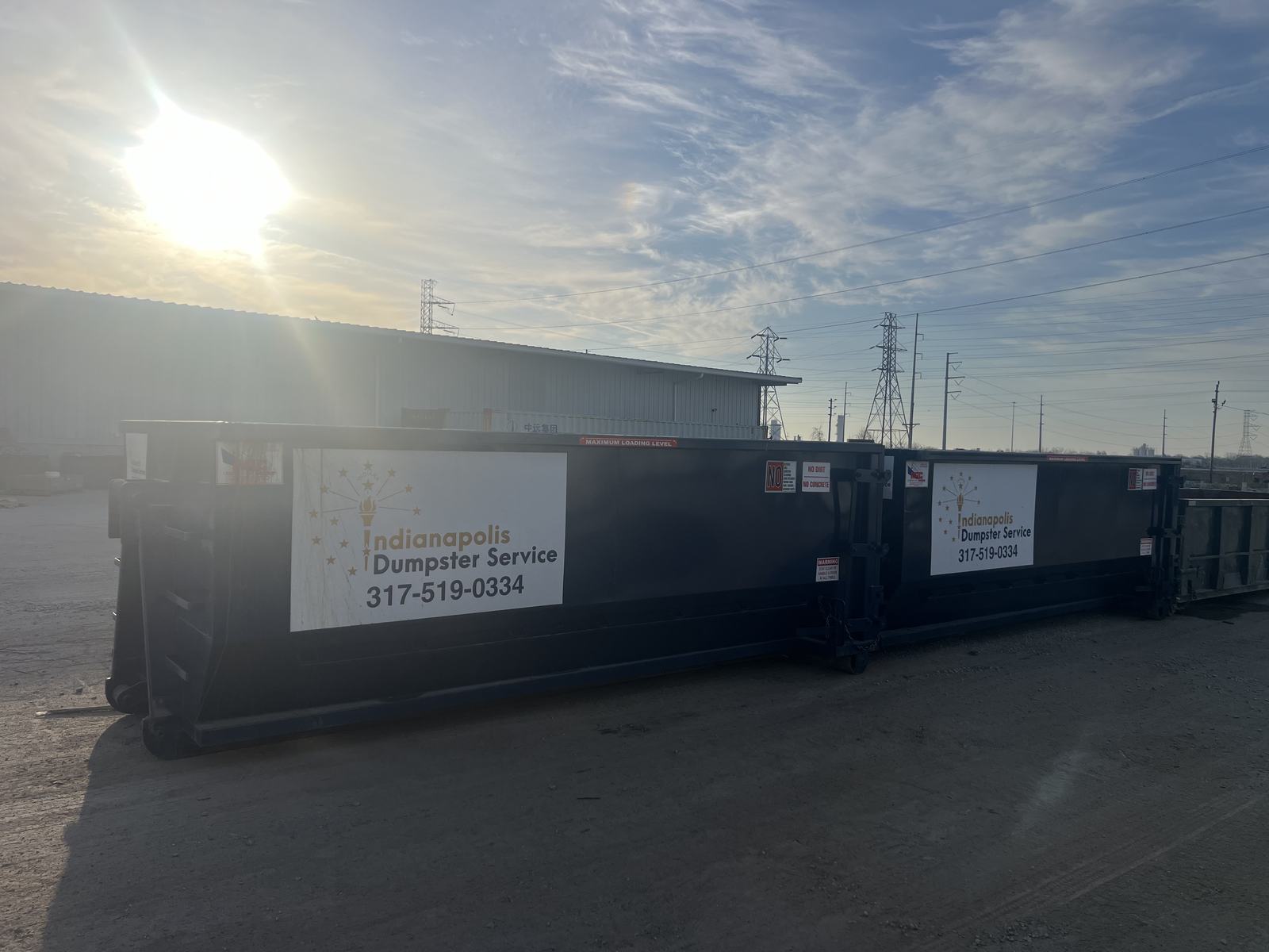 A navy Indianapolis Dumpster Service roll off container in Indianapolis. Two dumpsters on a commercial site at sunrise.