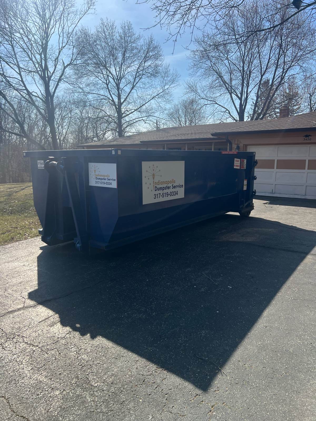 A navy Indianapolis Dumpster Service roll off container in Indianapolis. In front of a ranch home, front walk clear.