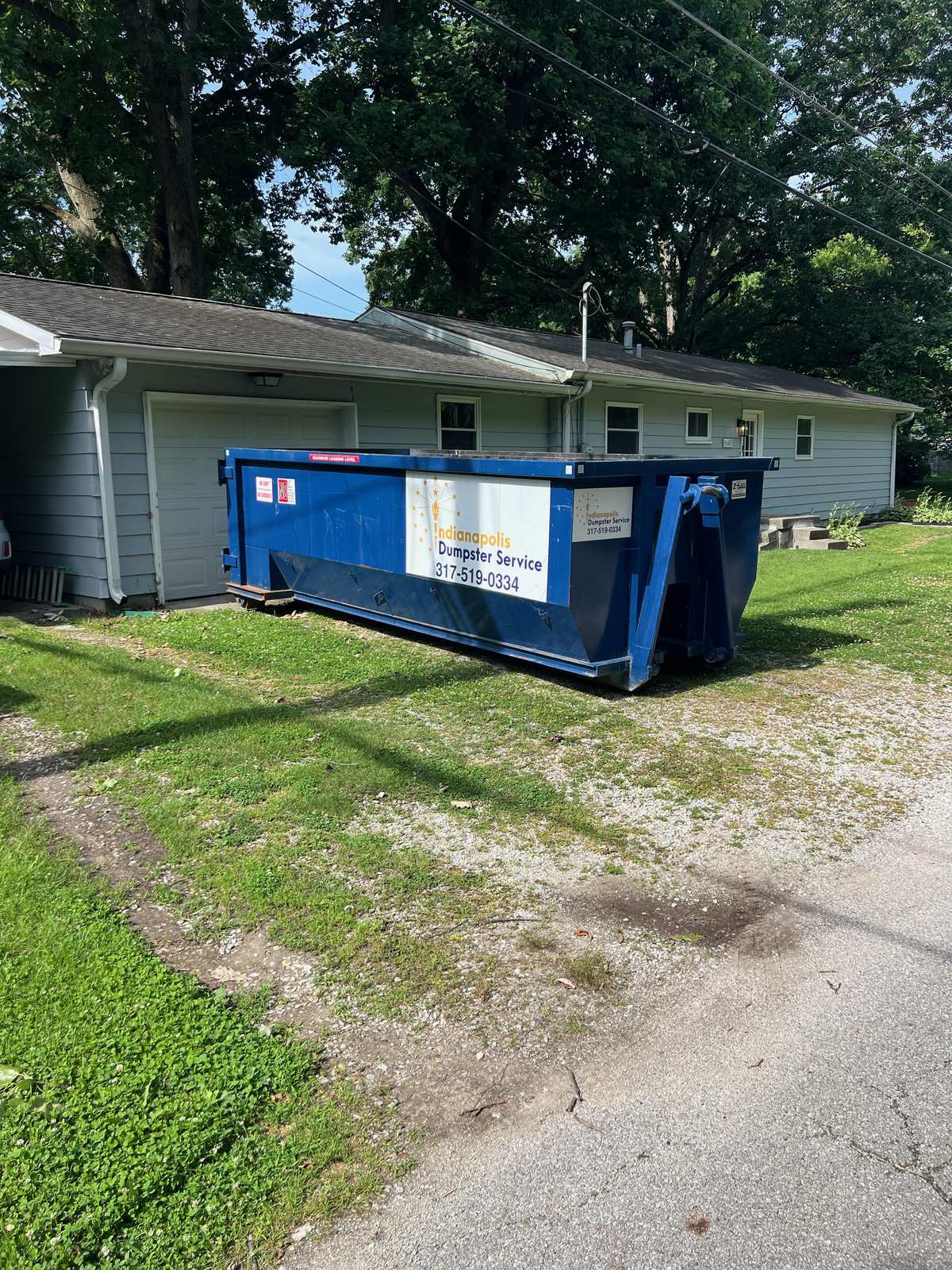 A navy Indianapolis Dumpster Service roll off container in Indianapolis. On the driveway of a ranch home.