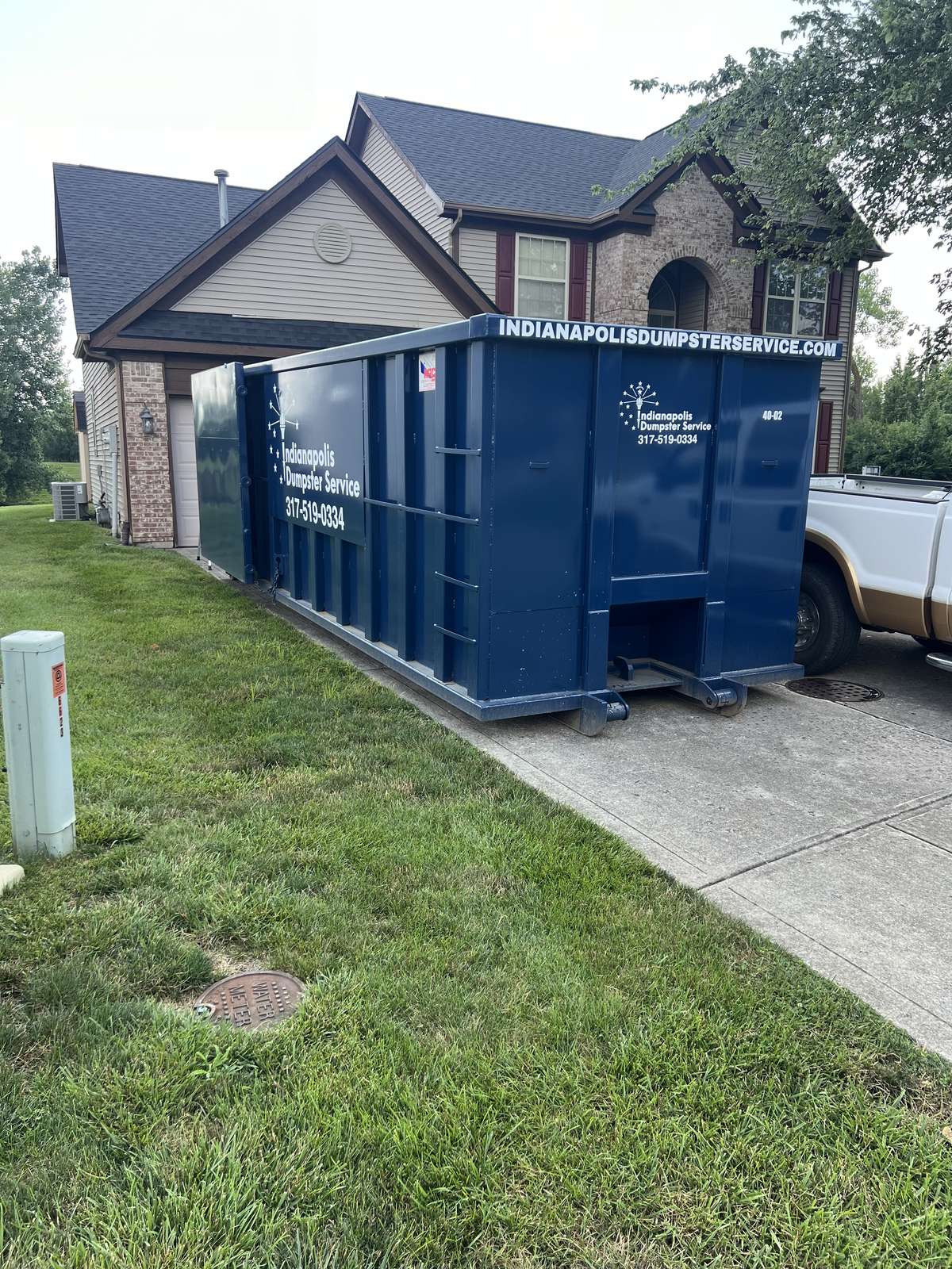 A navy Indianapolis Dumpster Service roll off container in Indianapolis. A tear-off in progress, dumpster beside the porch.