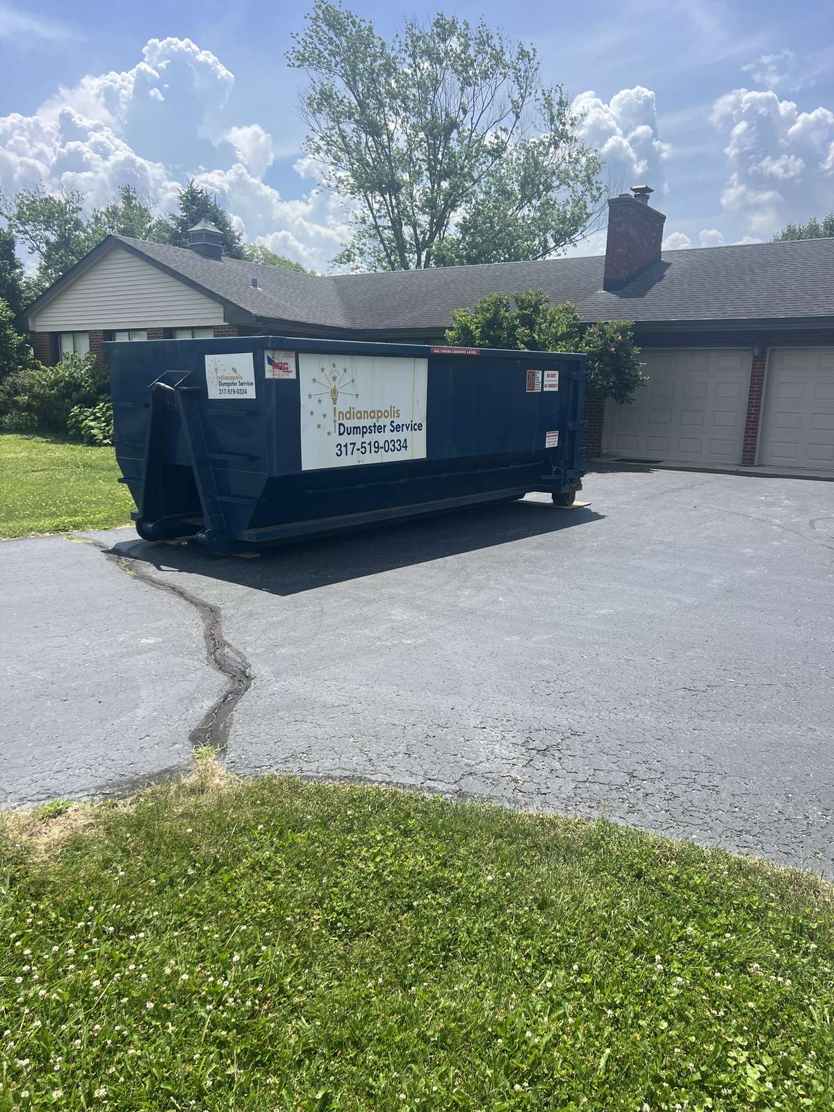 A navy Indianapolis Dumpster Service roll off container in Indianapolis. On a driveway under mature trees.