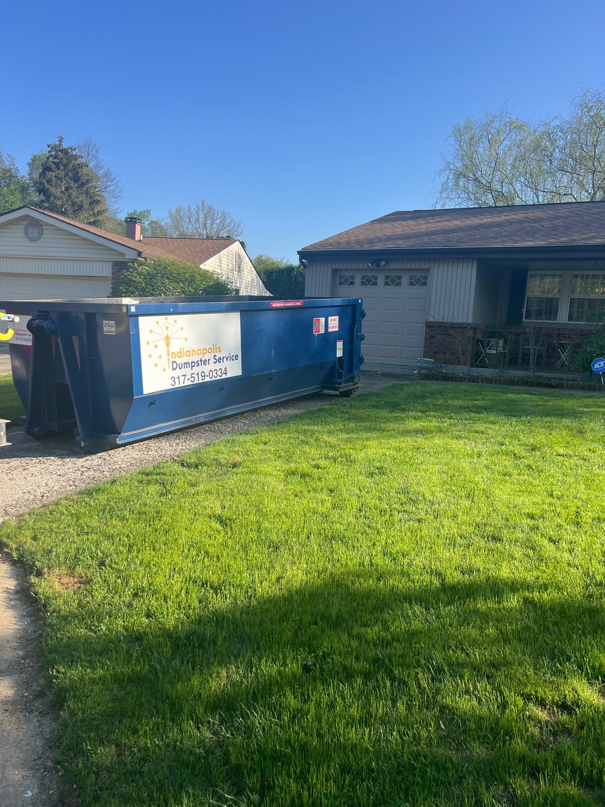 A navy Indianapolis Dumpster Service roll off container in Indianapolis. On the driveway of a one-story home.