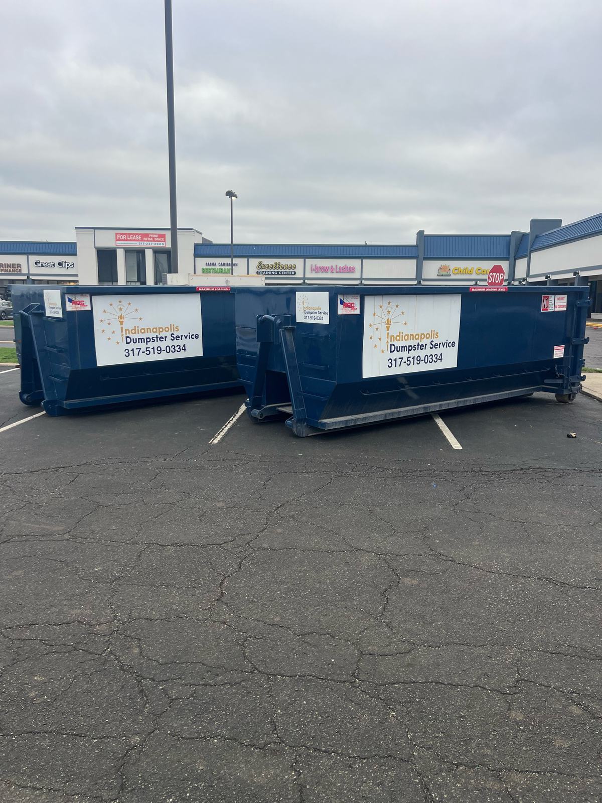 A navy Indianapolis Dumpster Service roll off container in Indianapolis. Two dumpsters in a shared lot.