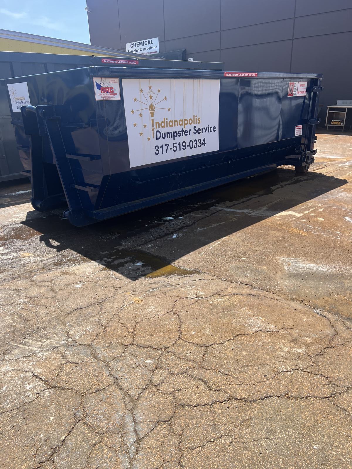 A navy Indianapolis Dumpster Service roll off container in Indianapolis. On the paved area behind a commercial unit.
