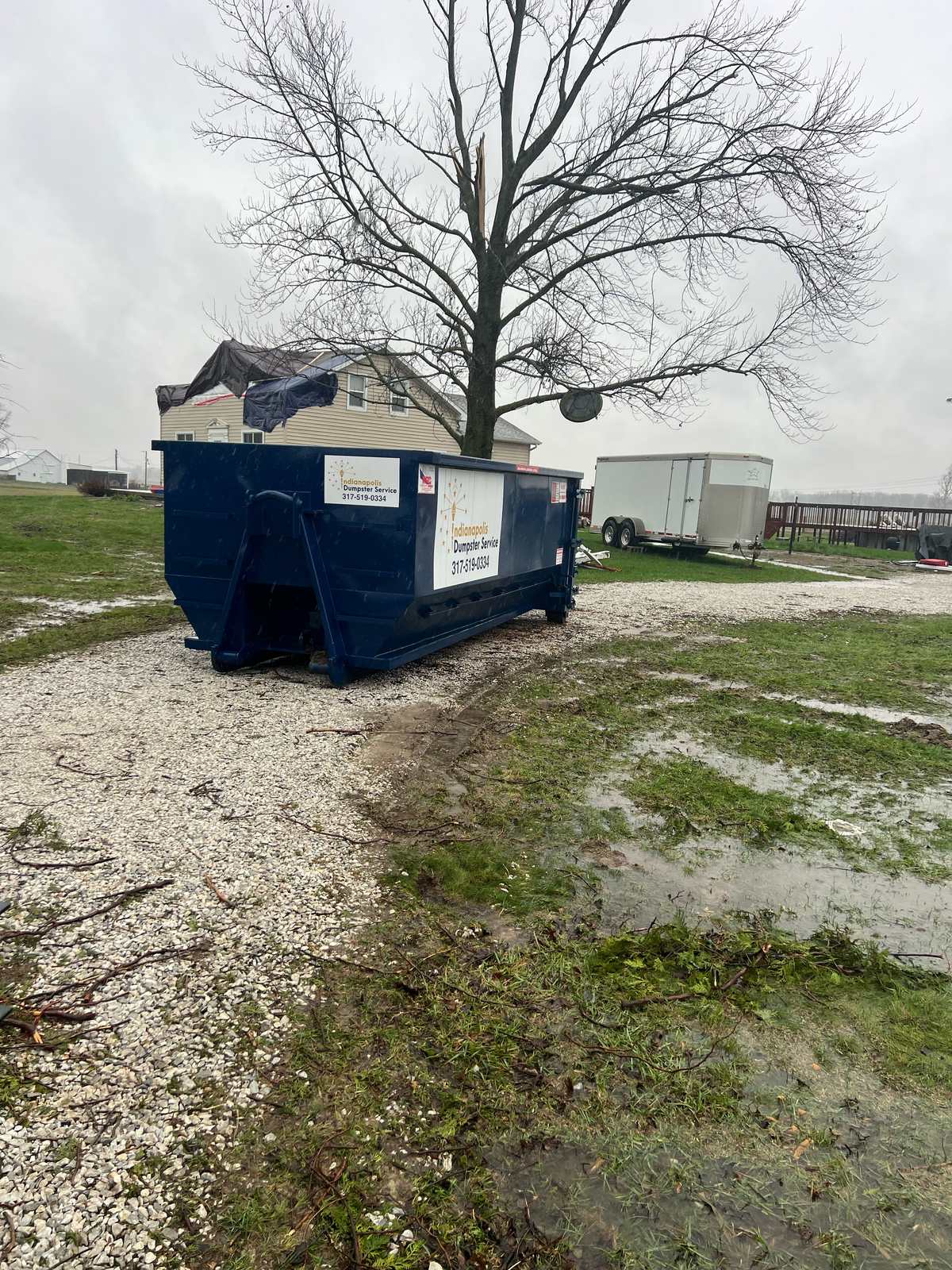 A navy Indianapolis Dumpster Service roll off container in Lapel. Beside an outbuilding.