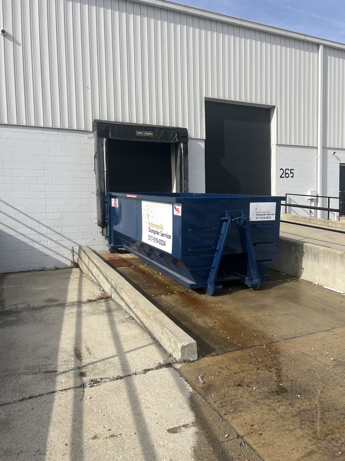 A navy Indianapolis Dumpster Service roll off container. At a loading dock door.