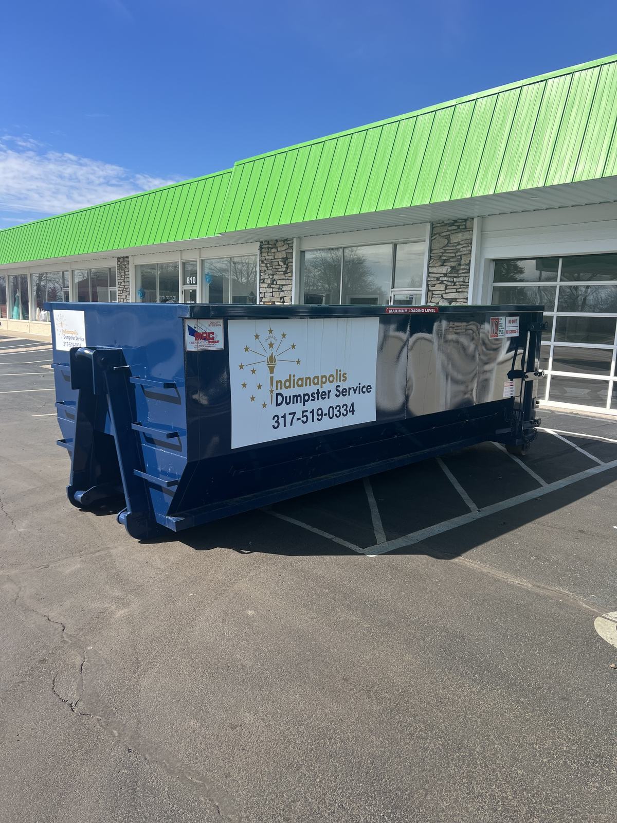 A navy Indianapolis Dumpster Service roll off container in Middletown. In front of a storefront.
