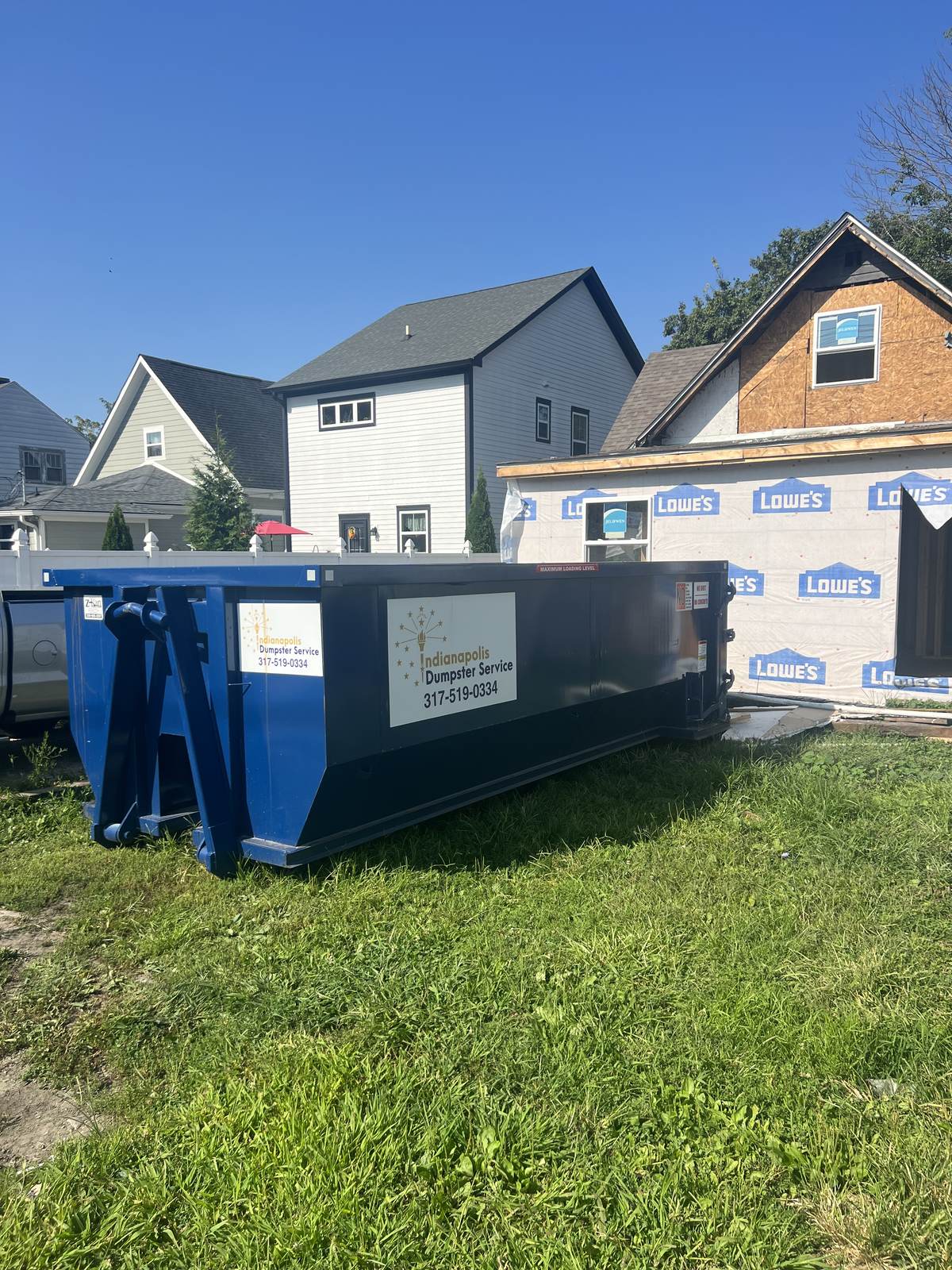 A navy Indianapolis Dumpster Service roll off container. A house in house wrap with the dumpster on site.