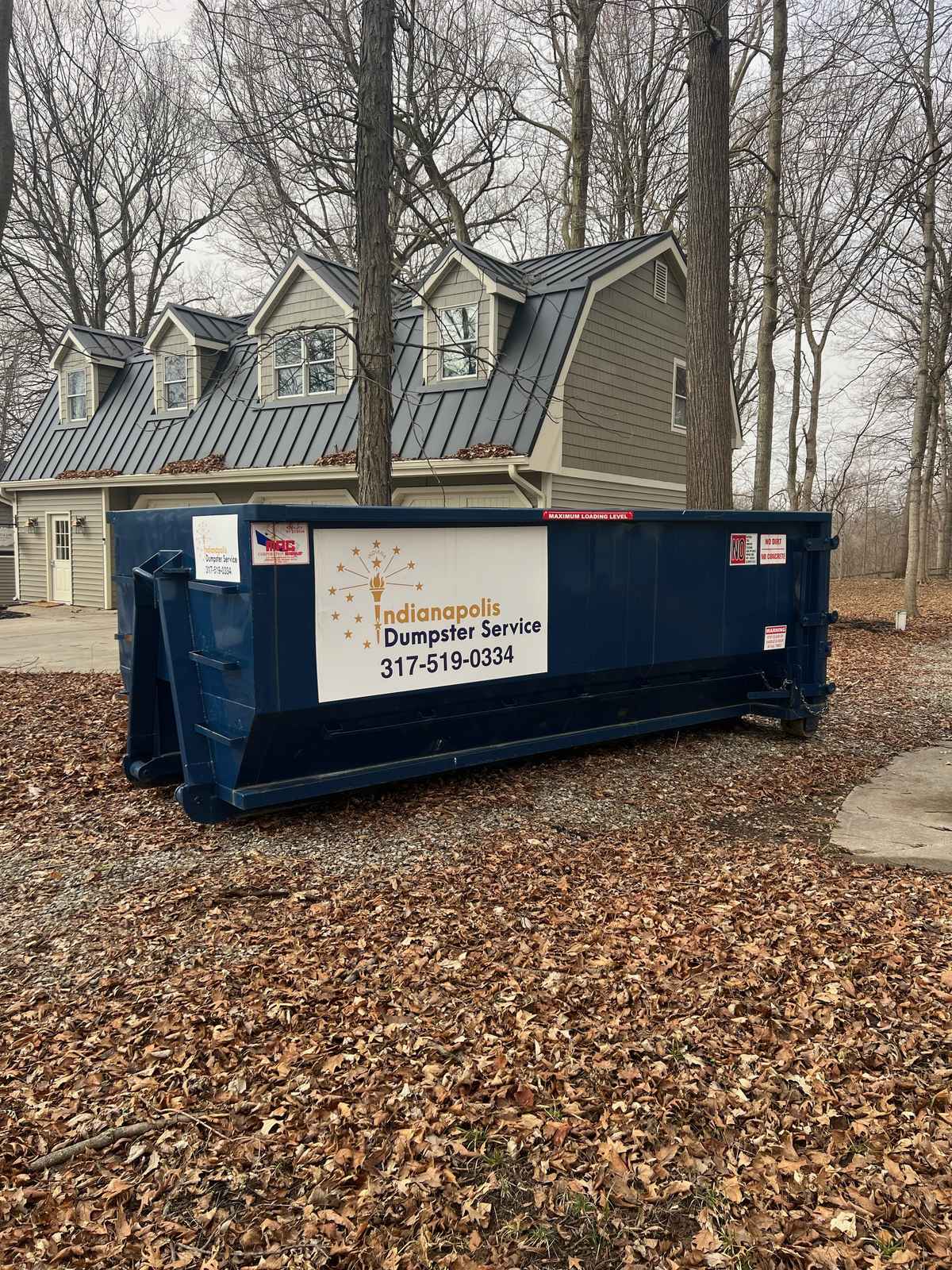 A navy Indianapolis Dumpster Service roll off container in Noblesville. Beside the front walk of a two-story home.