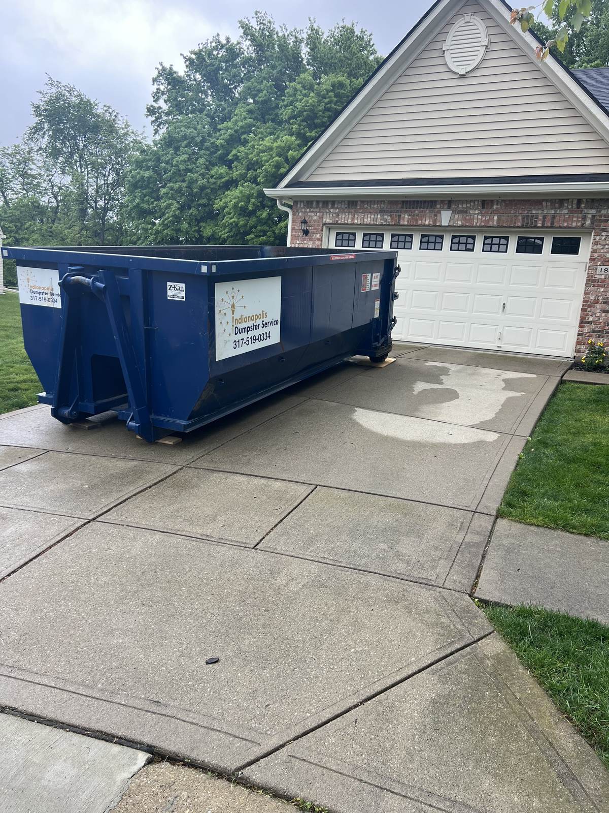 A navy Indianapolis Dumpster Service roll off container in Noblesville. On a wide driveway with the garage door clear.