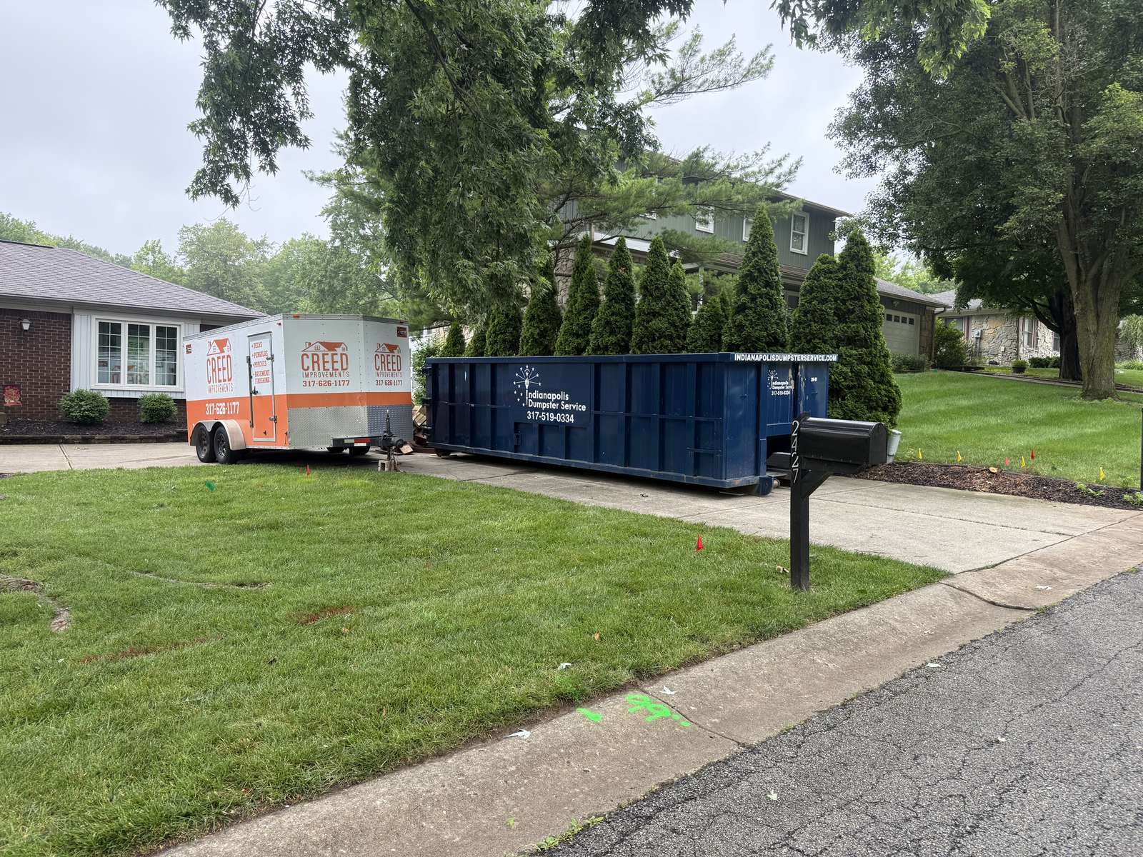 A navy Indianapolis Dumpster Service roll off container in Noblesville. A long driveway with room for the dumpster and a trailer.