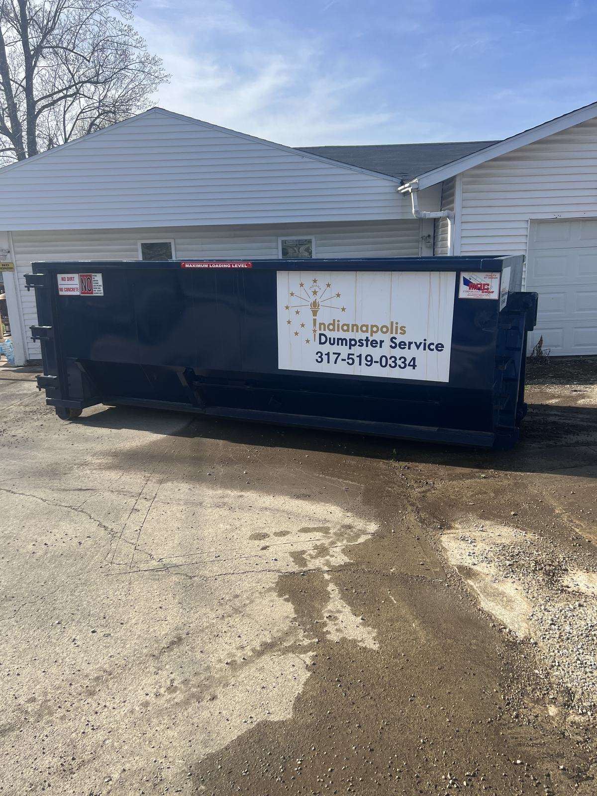 A navy Indianapolis Dumpster Service roll off container in Noblesville. On the driveway of a home with a metal roof.